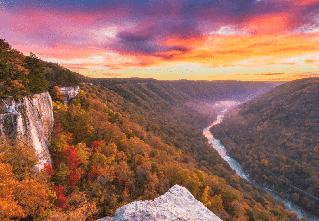 Scenic view of a river valley with autumn foliage and a colorful sunset sky.